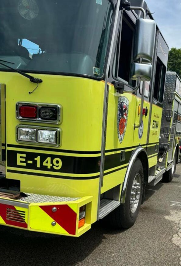 A bright yellow fire truck labeled "E-149" is parked on the street. The vehicle features various lights and equipment essential for firefighting and emergency responses. The weather appears to be clear and sunny.